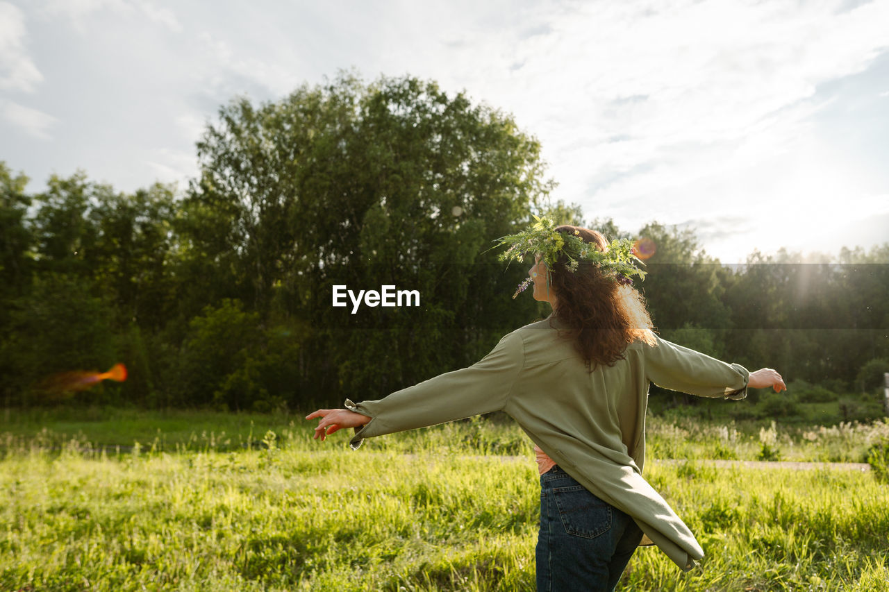 Female with floral crown dancing in green field outdoors, back view