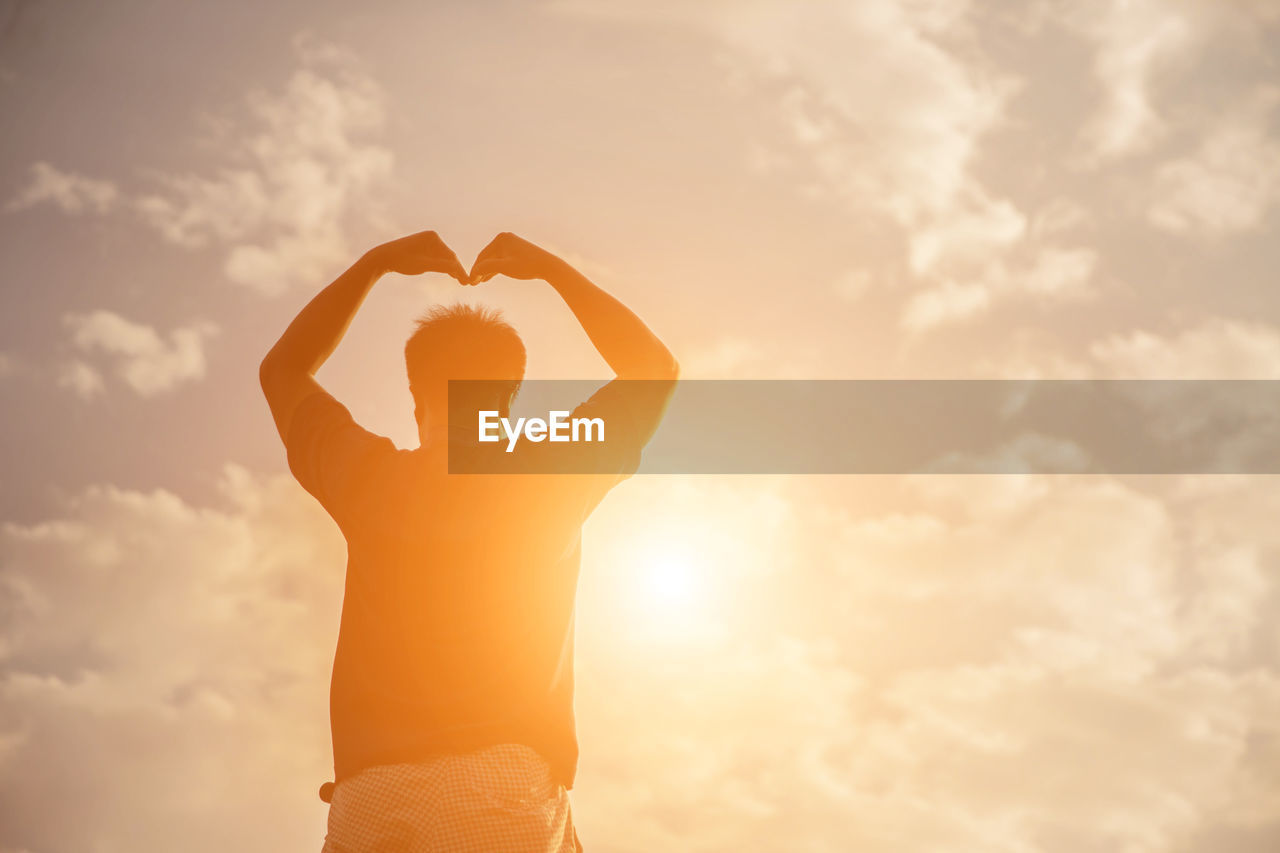 Silhouette man with arms raised standing against sky during sunset