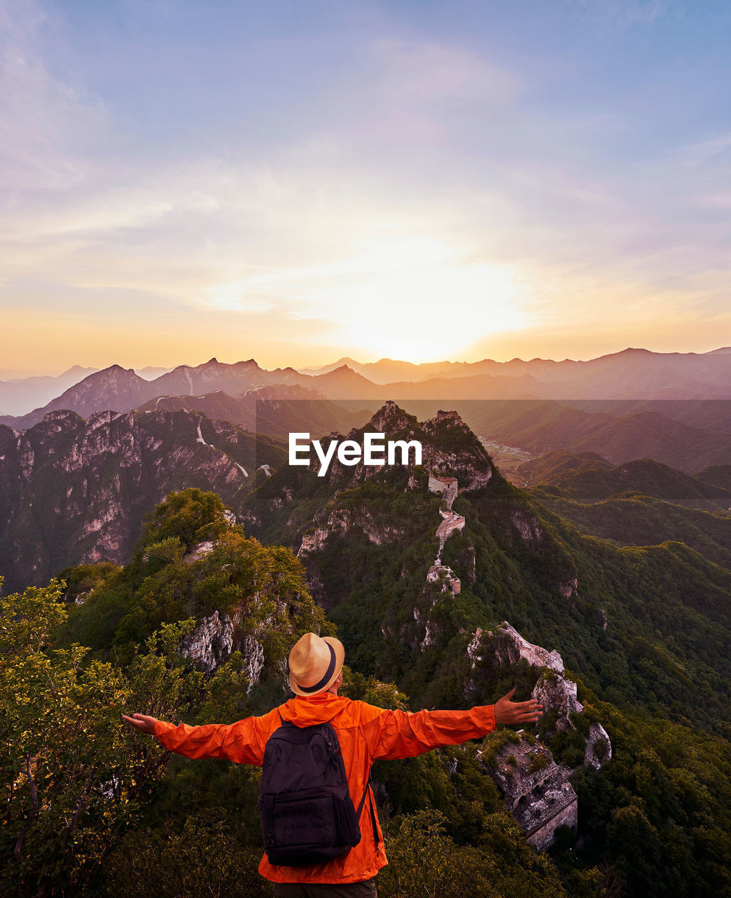 Rear view of man standing on mountain against sky during sunset