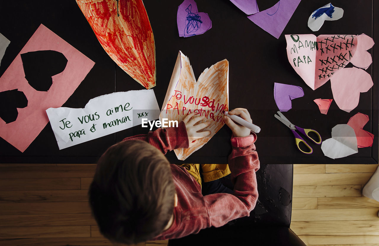 High angle view of boy writing on colorful papers at table