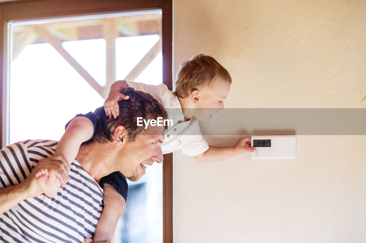 Father carrying son on shoulders, adjusting thermostat