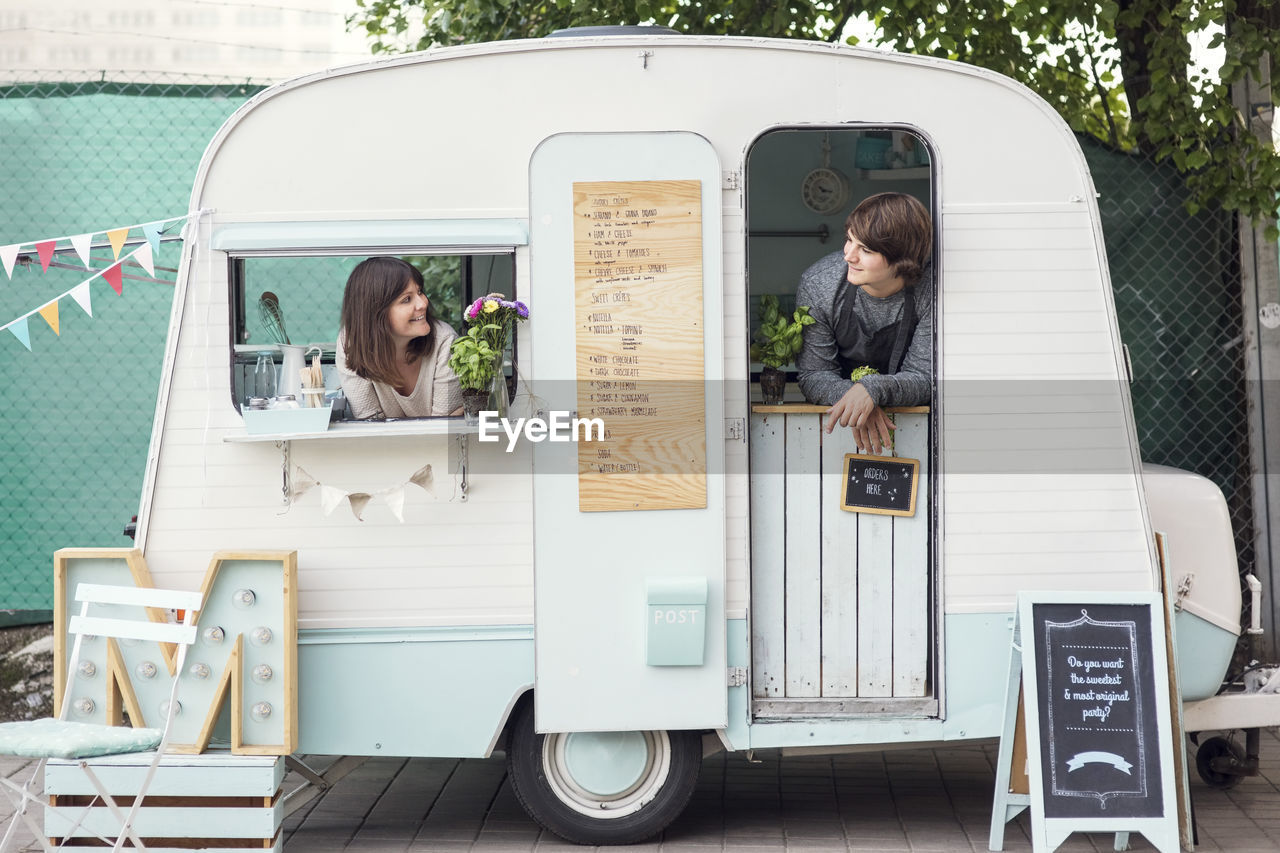 Male and female owners looking at each other while peeking through food truck windows