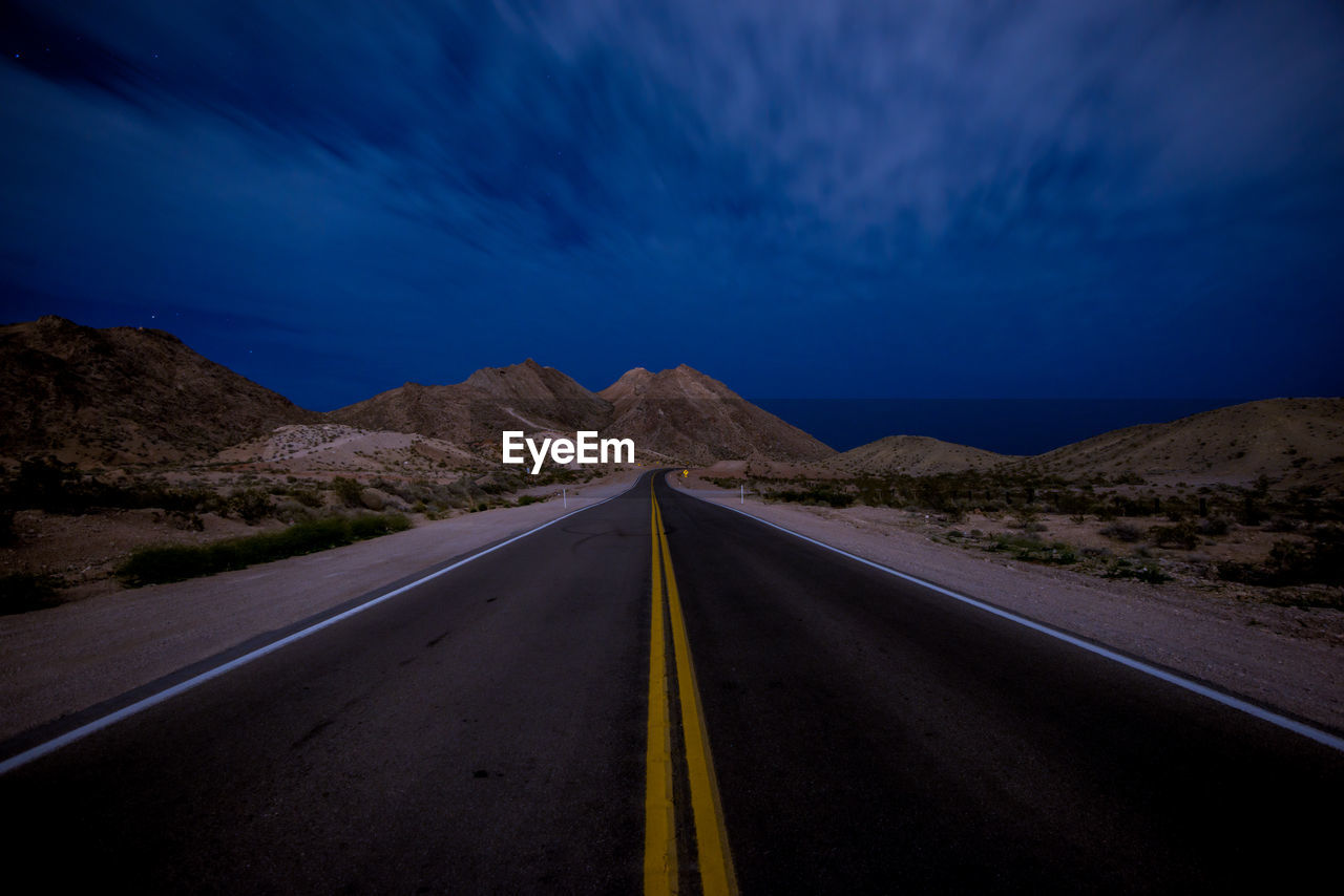 Road amidst landscape against sky at night leading to the mountains 