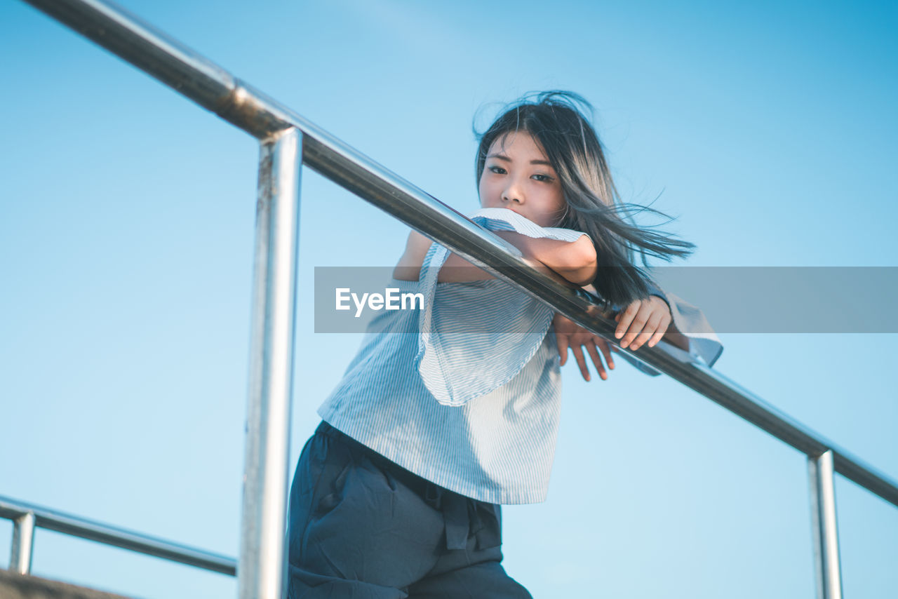 Portrait of young woman on footbridge against clear sky