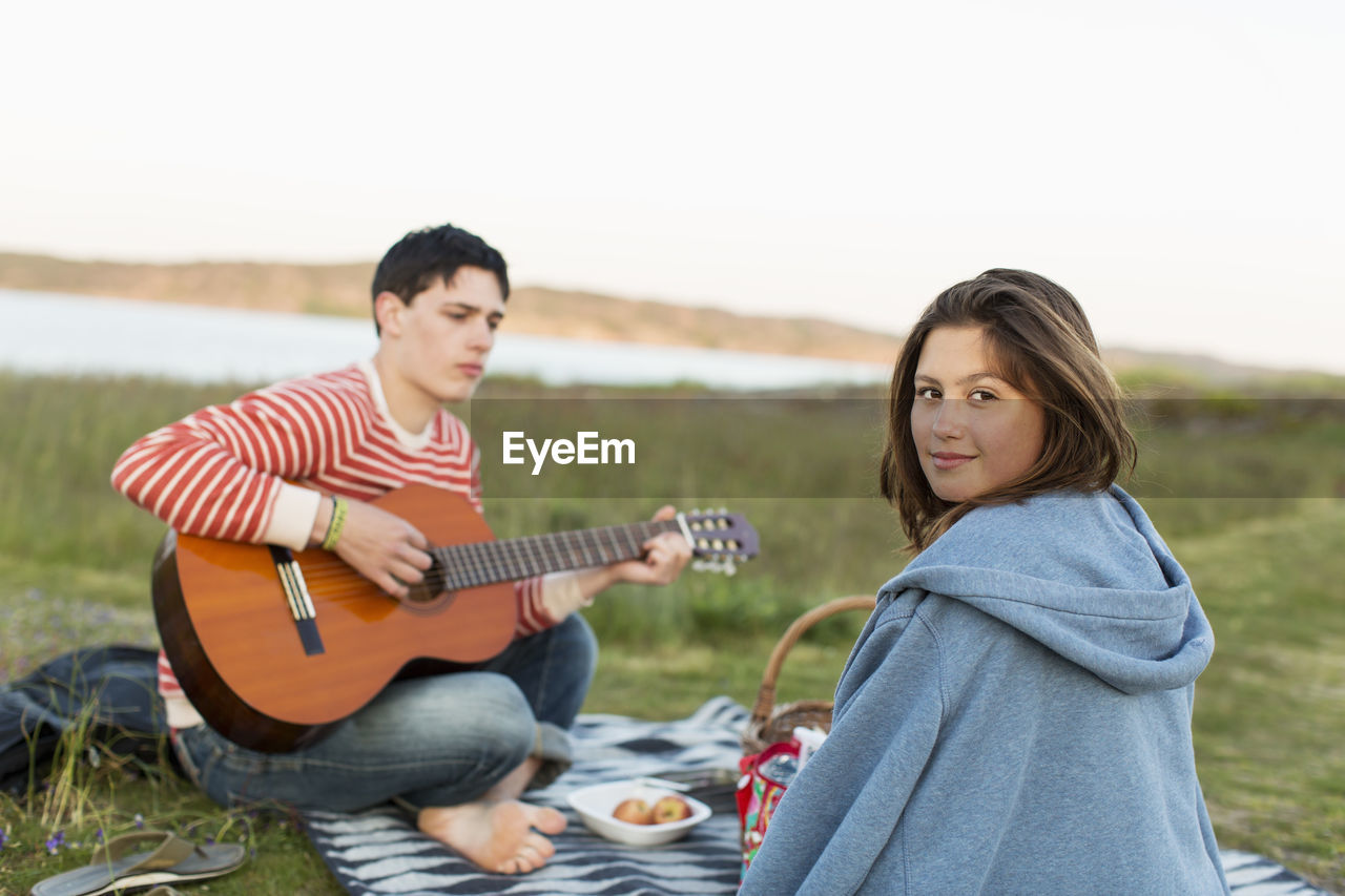 Rear view portrait of teenage girl with boyfriend playing guitar during picnic