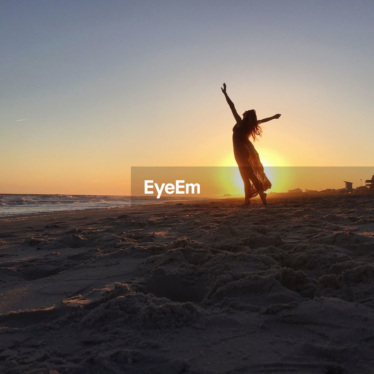 Silhouette mid adult woman jumping at beach against clear sky during sunset