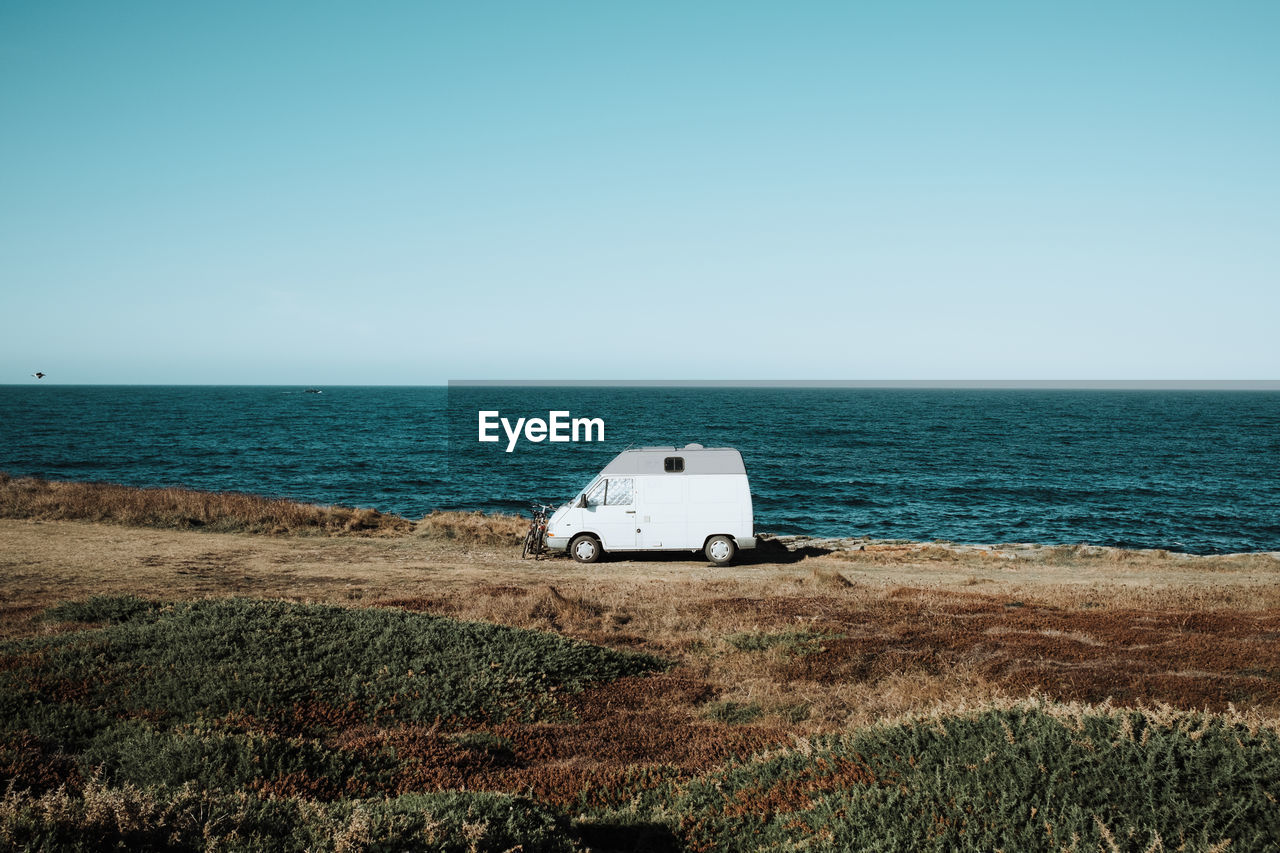 Scenic view of sea against clear blue sky with camping van