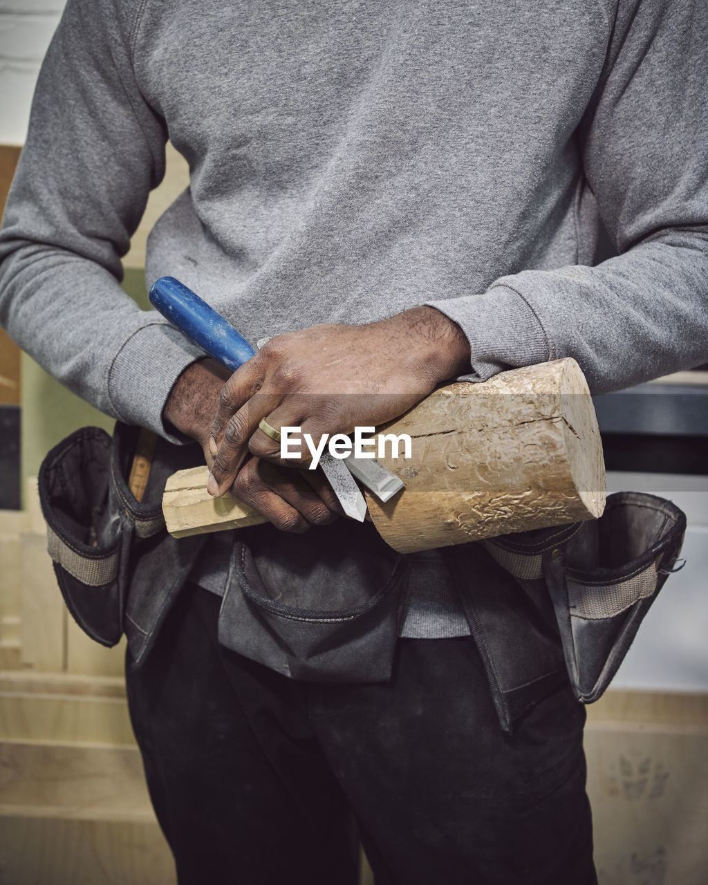 Midsection of carpenter holding wood and chisel