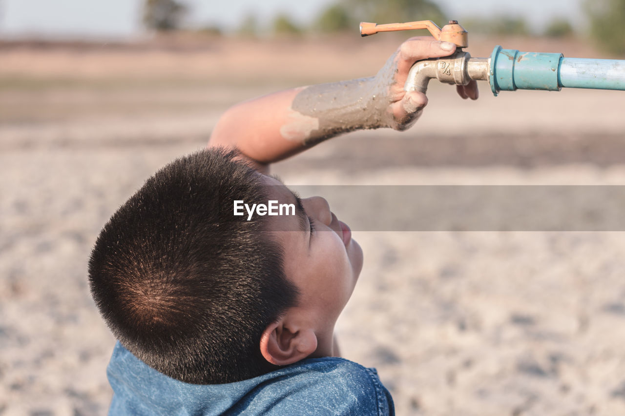 Close-up of boy looking at faucet during drought on field