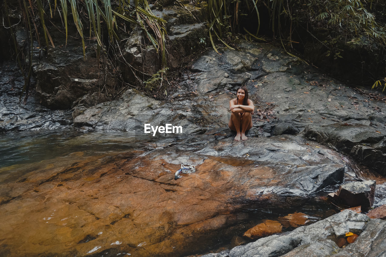 Full length of shirtless man standing on rock in river