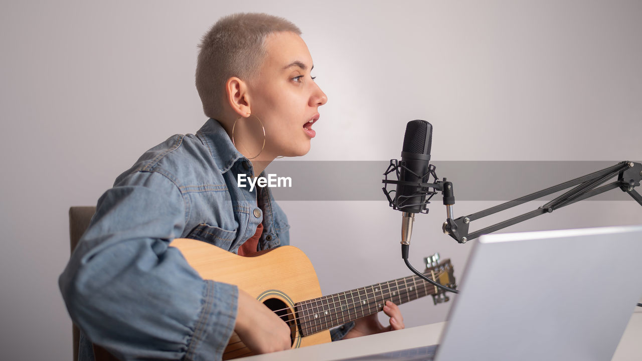 Full length of man playing guitar against wall