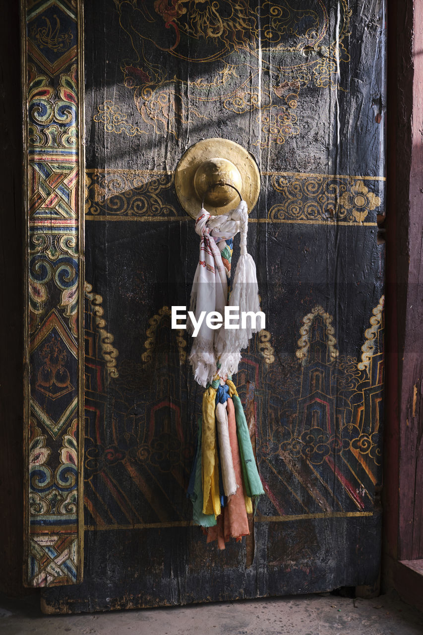 Part of old ancient tibetan building with wooden gate painted in various ornaments with golden handle with ritual ribbons