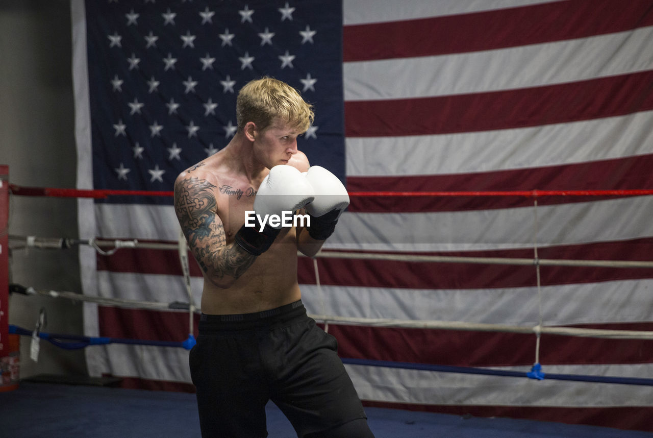 Shirtless boxer practicing in boxing ring against american flag