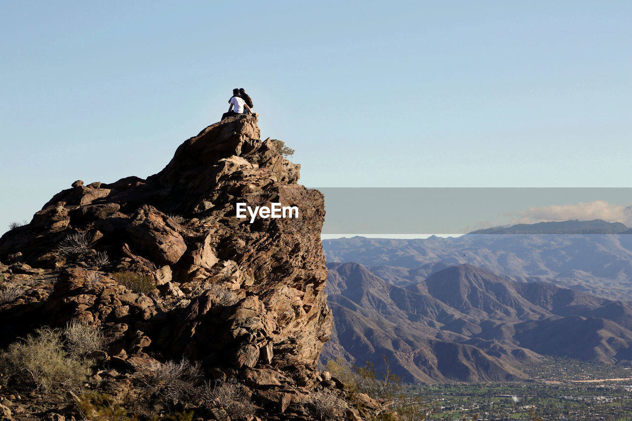 Couple sitting on mountain top in desert embracing