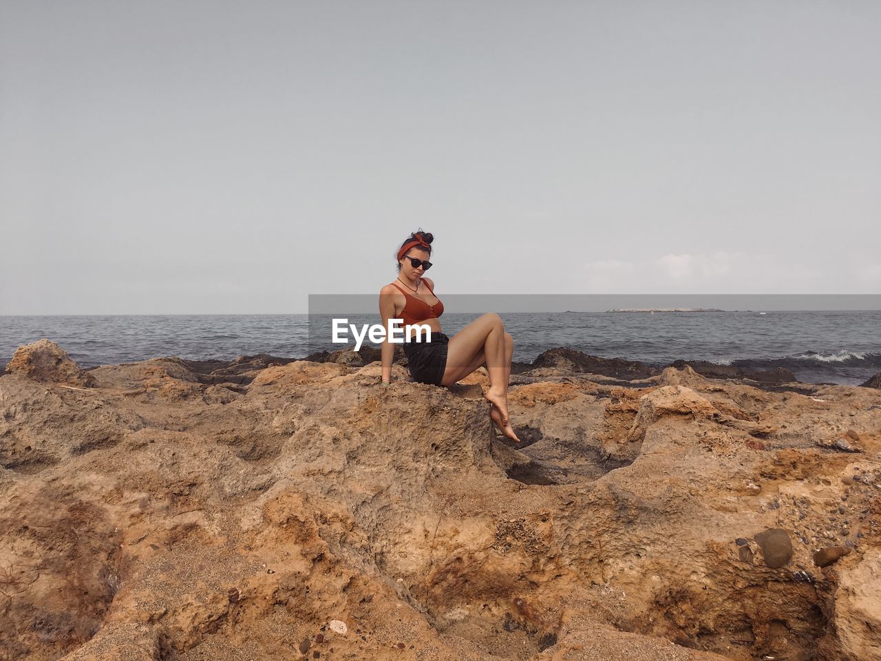 Portrait of woman sitting on rock at beach against sky