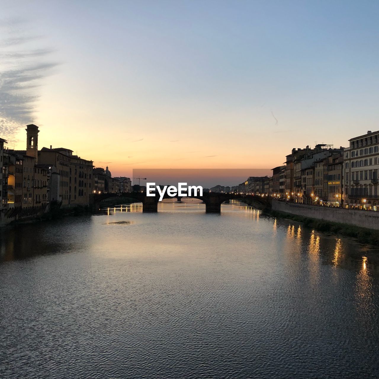 Bridge over river against buildings in city at sunset