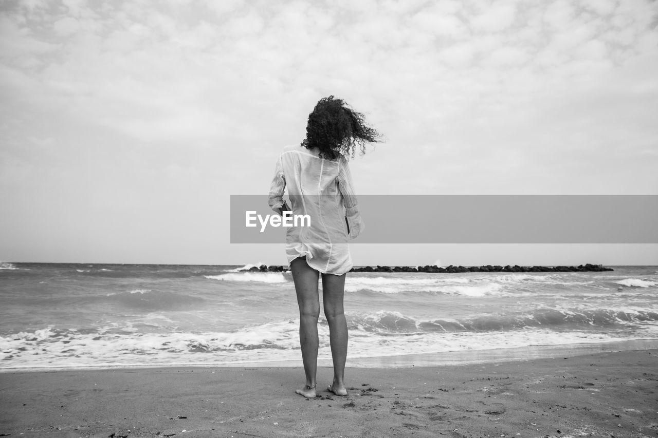 Rear view of woman standing on shore at beach against sky