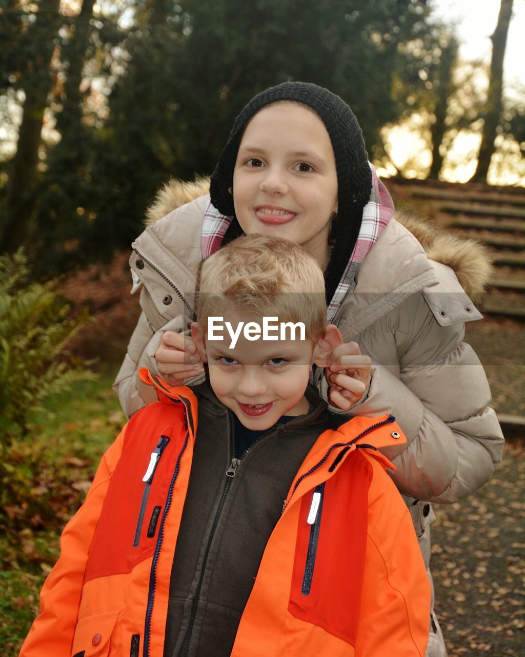 Portrait of girl pulling brother ears at park during sunset