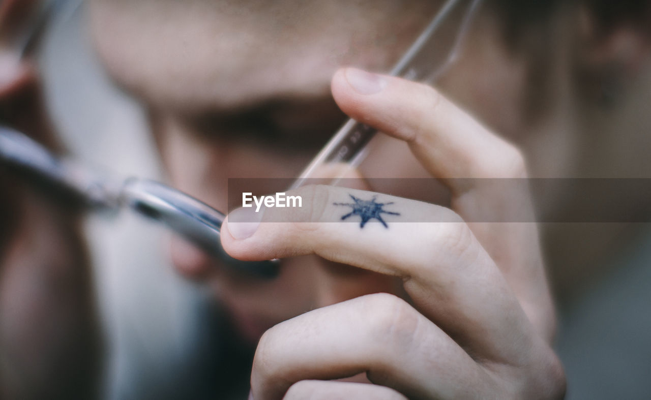 Close-up of teenage boy with tattoo holding eyeglasses