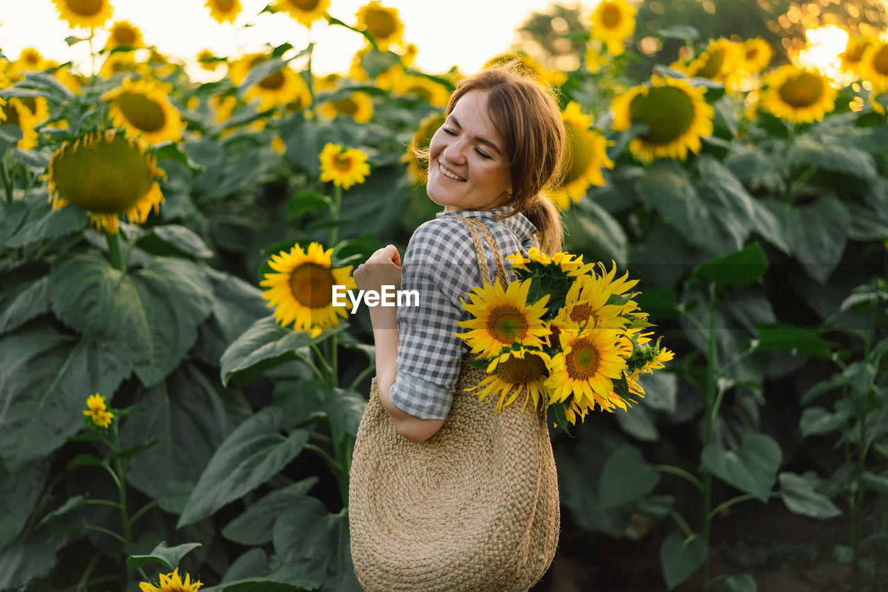 Beautiful young woman with sunflowers enjoying nature and laughing on summer sunflower field.