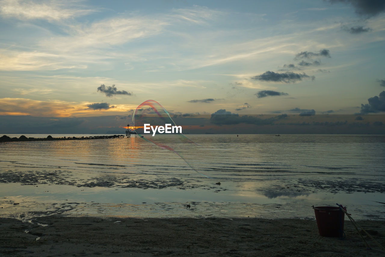 Soap bubble over sea against sky during sunset