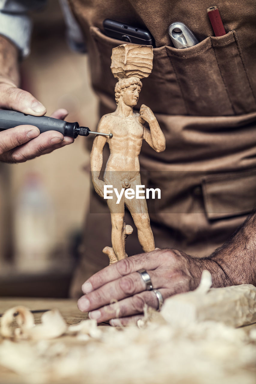 Midsection of carpenter carving on figurine in workshop