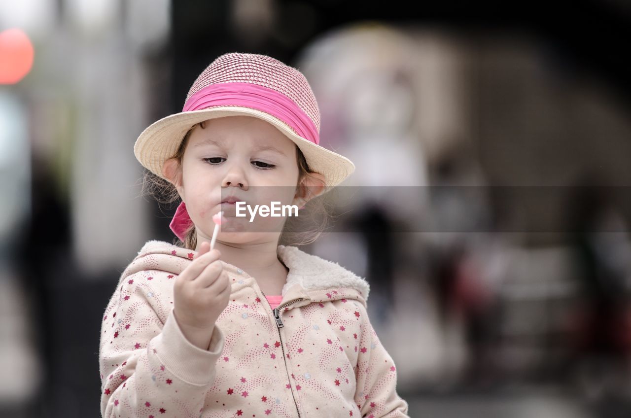Girl wearing hat while looking at lollipop