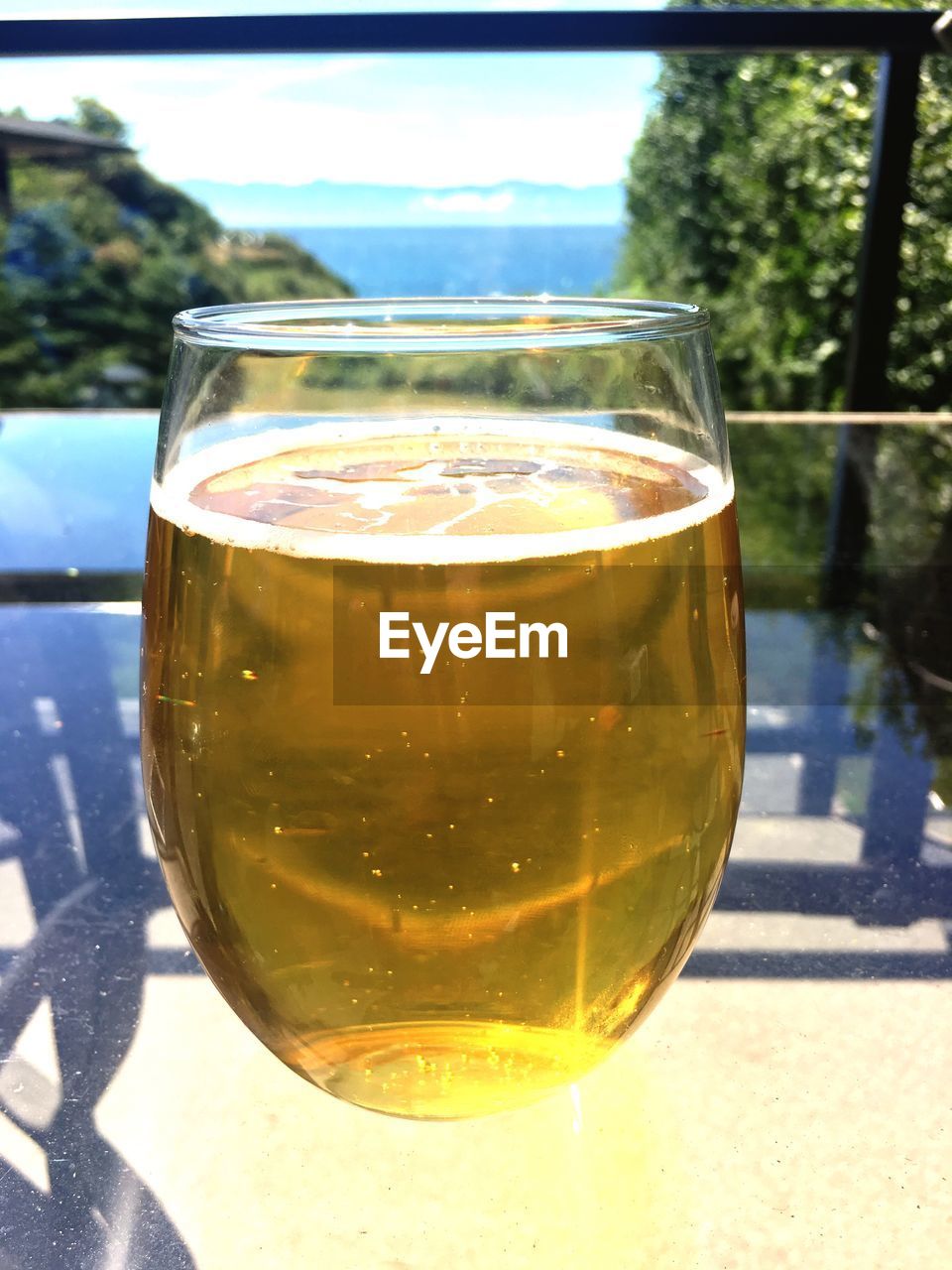 CLOSE-UP OF BEER IN GLASS ON TABLE AGAINST TREES