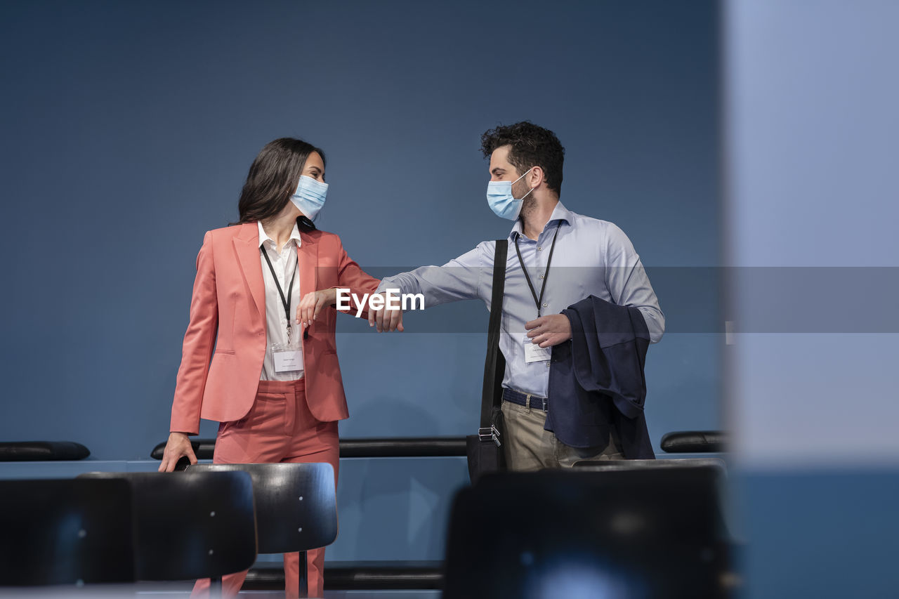 Colleagues with protective face mask bumping elbows in office