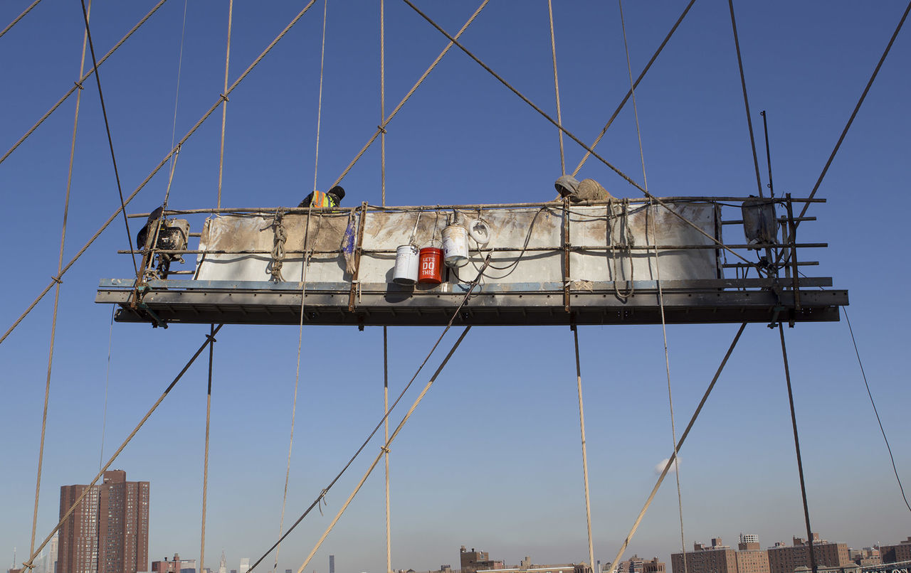 Low angle view of workers amidst bridge steel cables against clear blue sky
