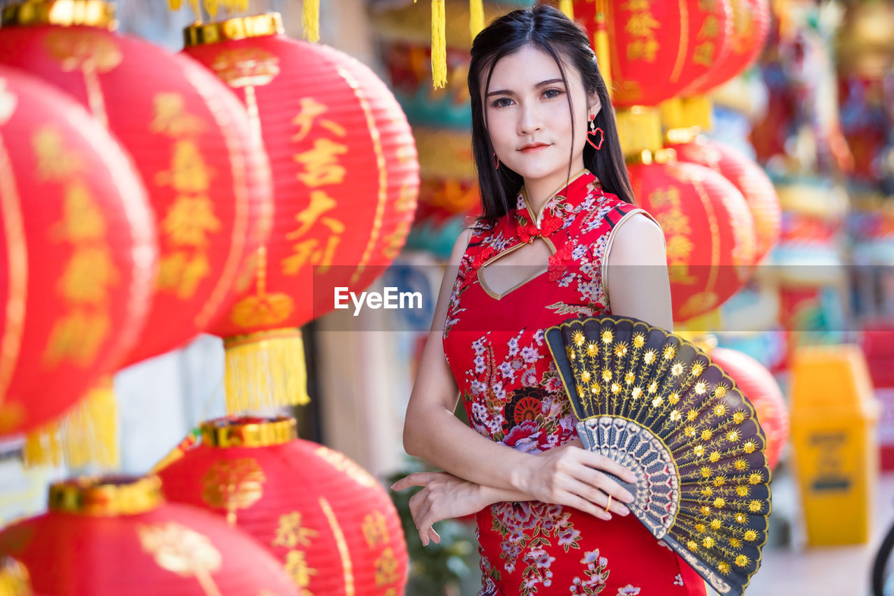 PORTRAIT OF YOUNG WOMAN WITH RED UMBRELLA STANDING IN TRADITIONAL CLOTHING