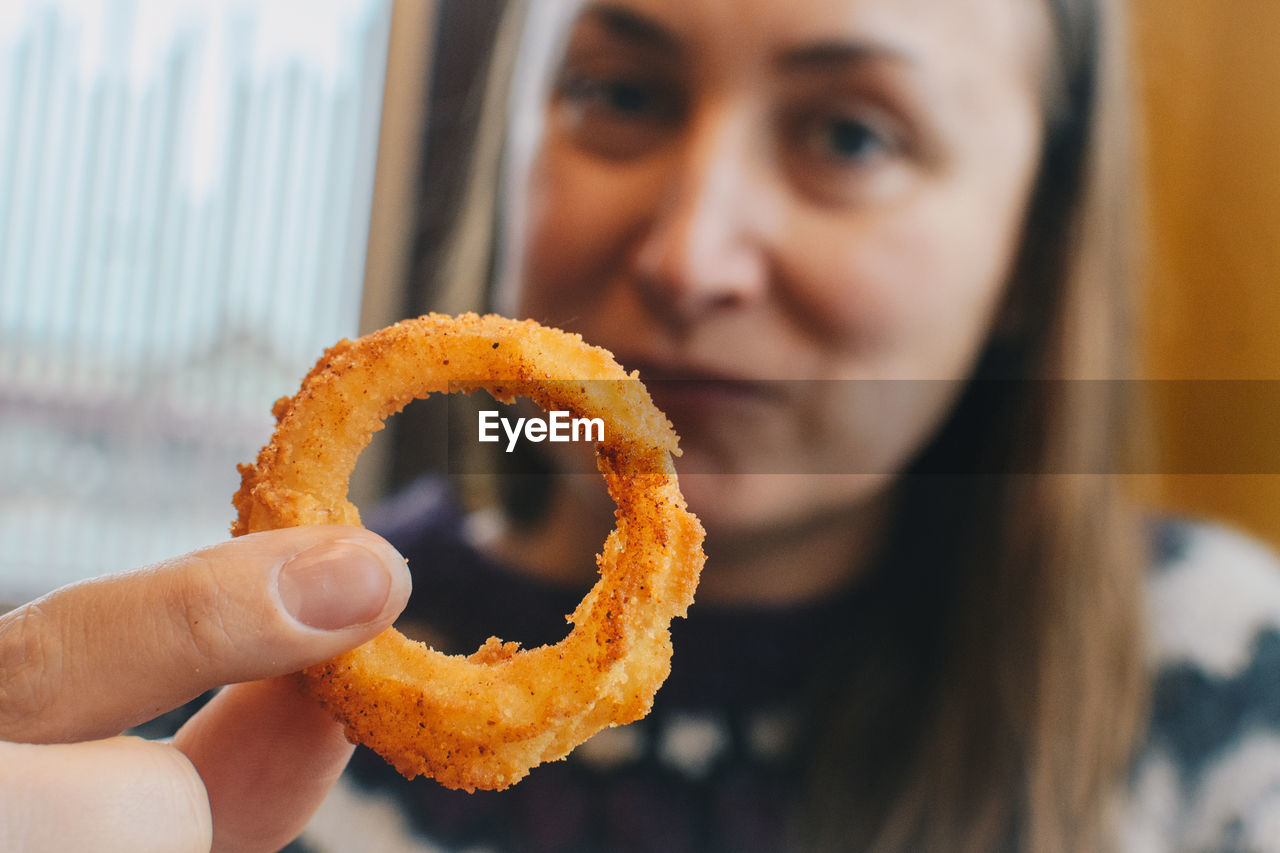 Portrait of woman holding onion ring while sitting at cafe