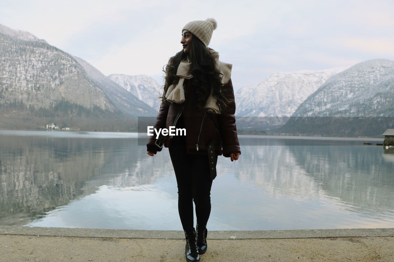 Full length of woman standing by lake against mountain during winter