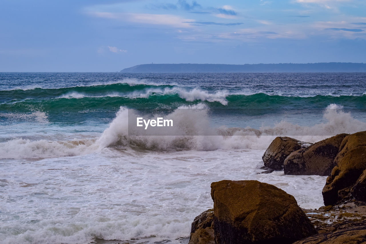 sea, water, wave, motion, rock, shore, body of water, beach, land, sky, ocean, beauty in nature, wind wave, sports, water sports, surfing, scenics - nature, coast, nature, horizon, power in nature, breaking, horizon over water, cloud, sand, terrain, splashing, vacation, outdoors, cliff, environment, day, hitting, coastline, travel destinations