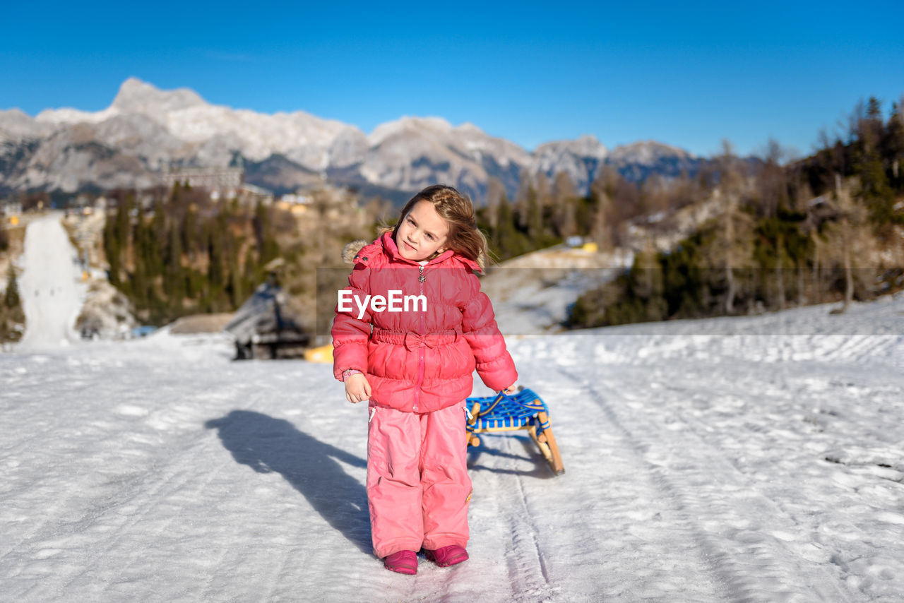 Girl pulling sled on snow against sky