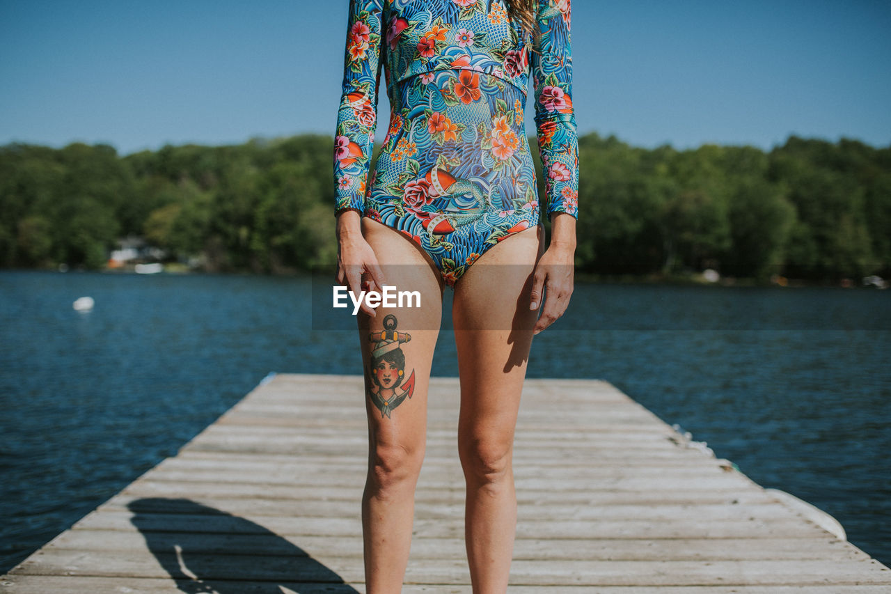 Midsection of woman standing on pier over lake against sky