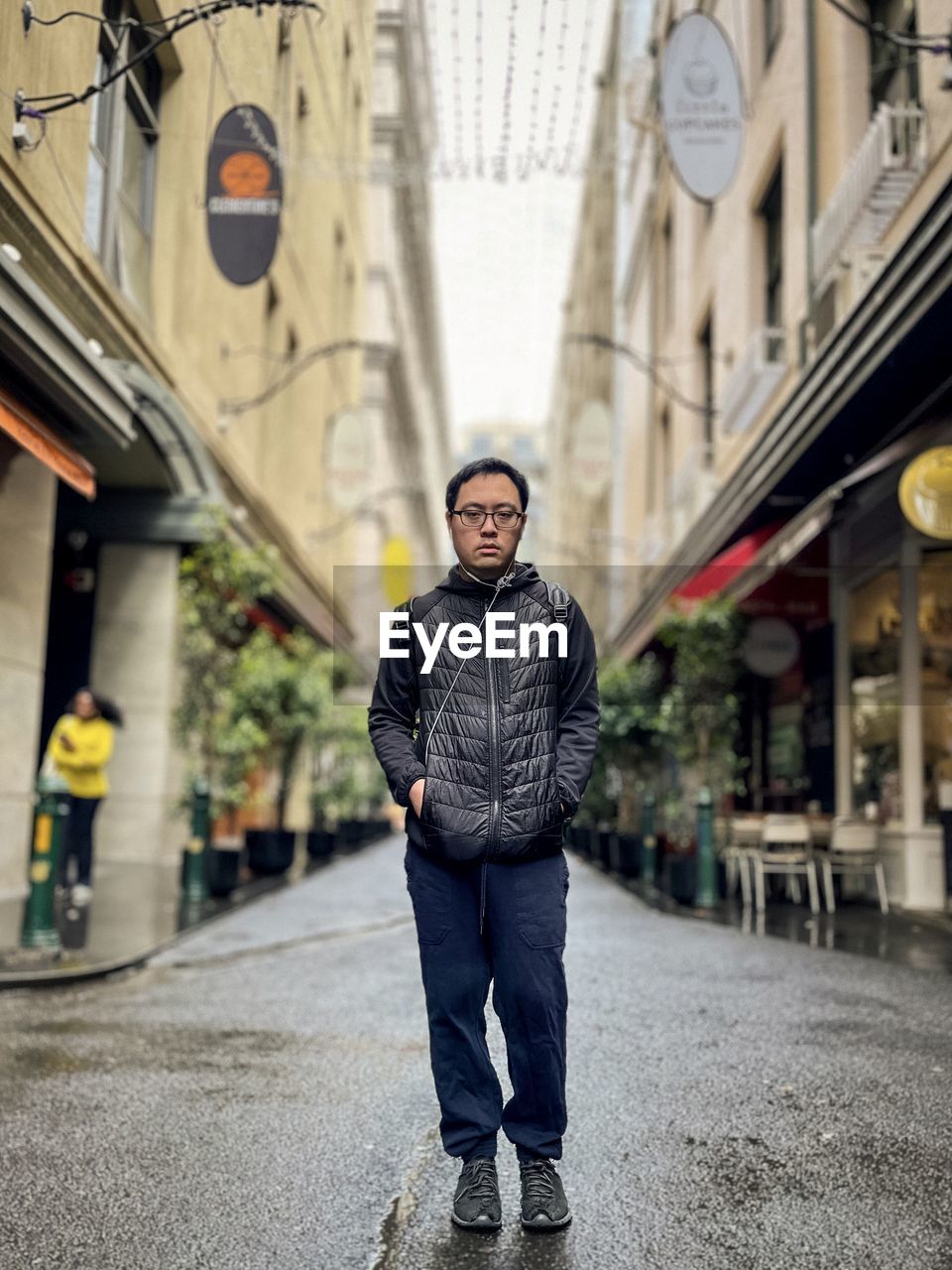 Full length of asian man standing in laneway against buildings in the city.