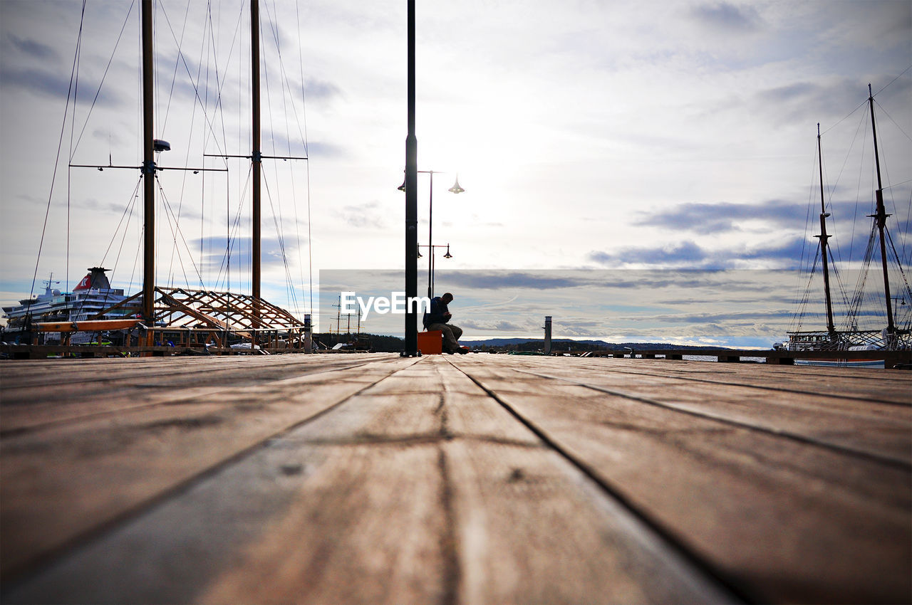 Distance view of man sitting on pier against sky