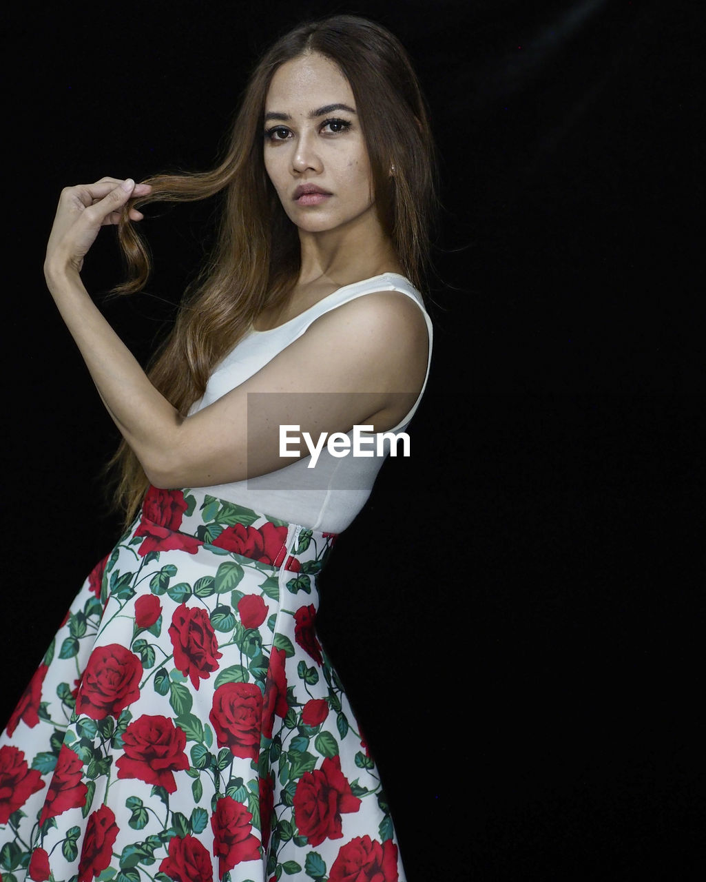 Portrait of young woman standing against black background