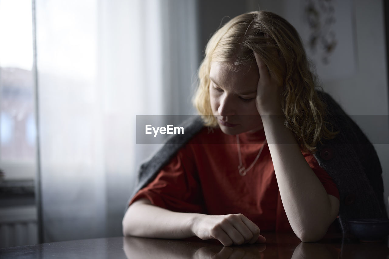 Pensive teenage girl sitting at table with head in hands