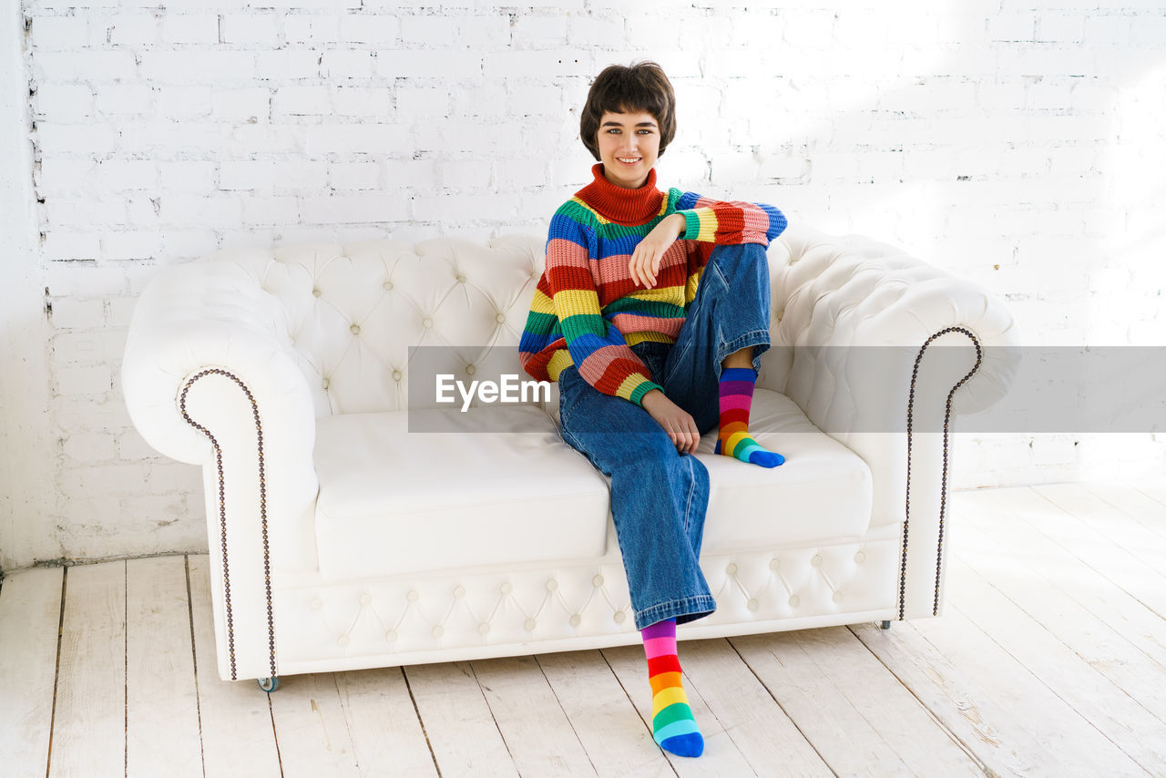 Portrait of man sitting on sofa against wall at home