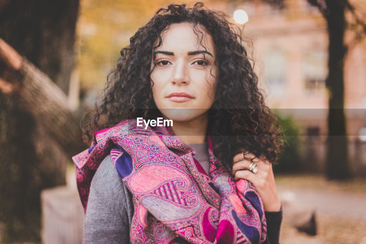 Close-up portrait of young woman with curly hair standing outdoors