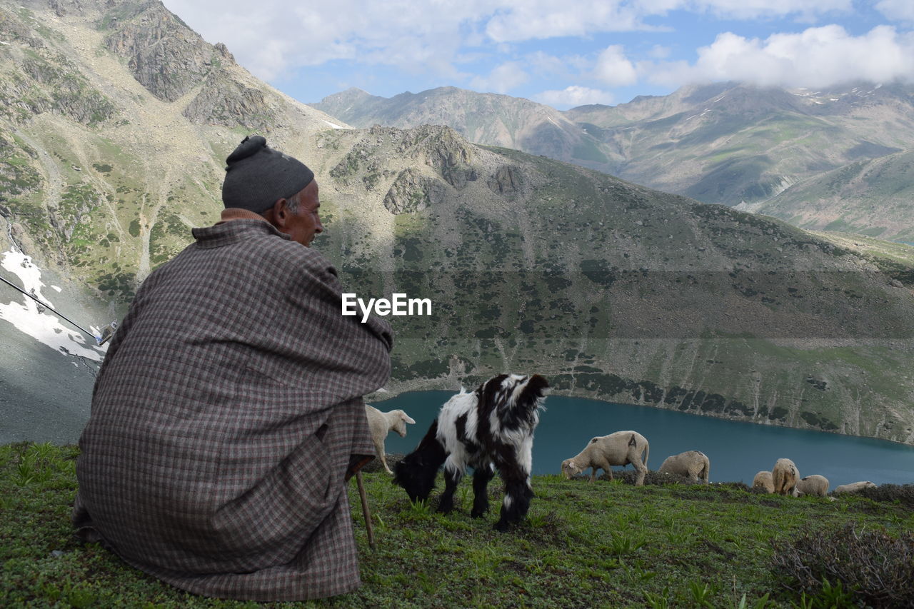 Man with sheep sitting on field against mountains