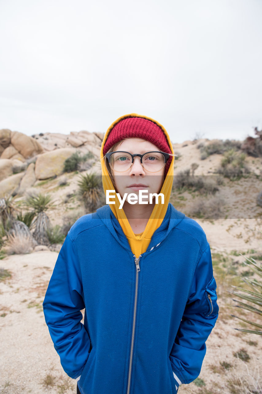 Tween with beanie and glasses in front of small mound in desert