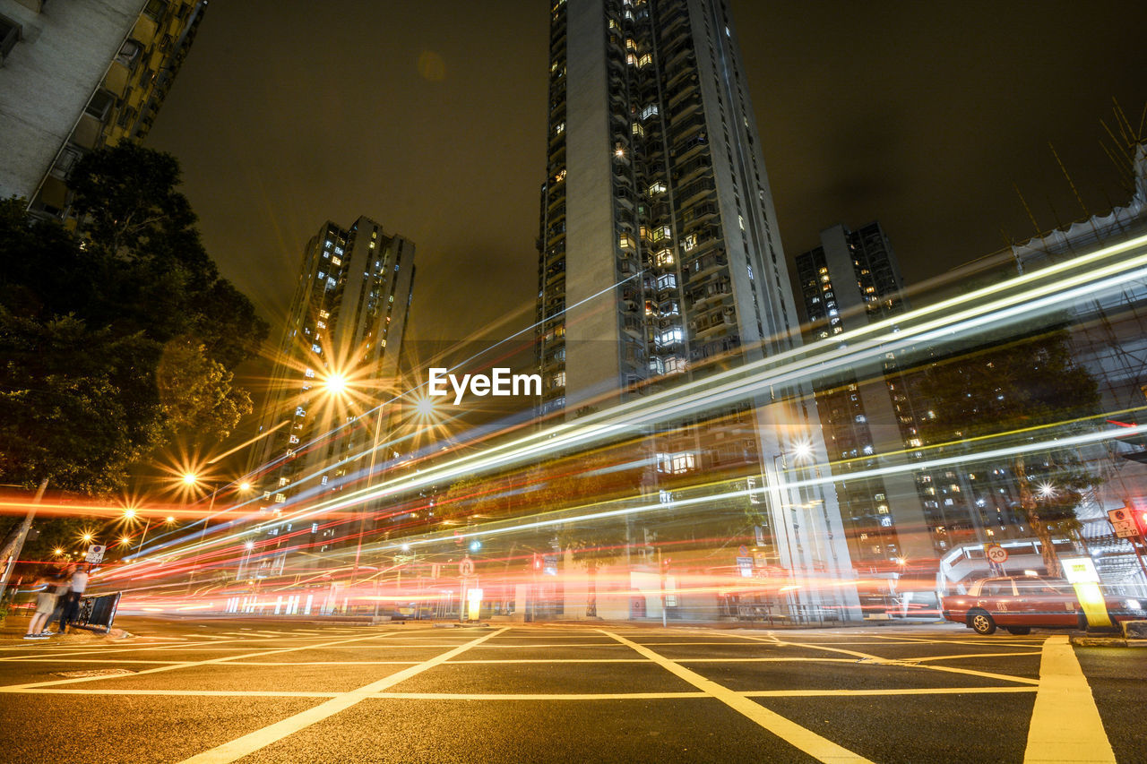 Light trails on city street by buildings against sky at night in hong kong 