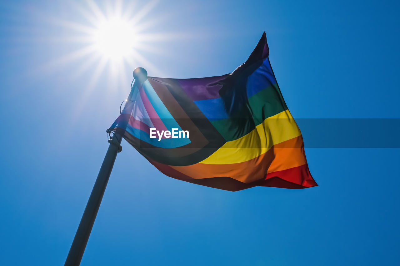 Low angle view of progress pride flag against blue sky