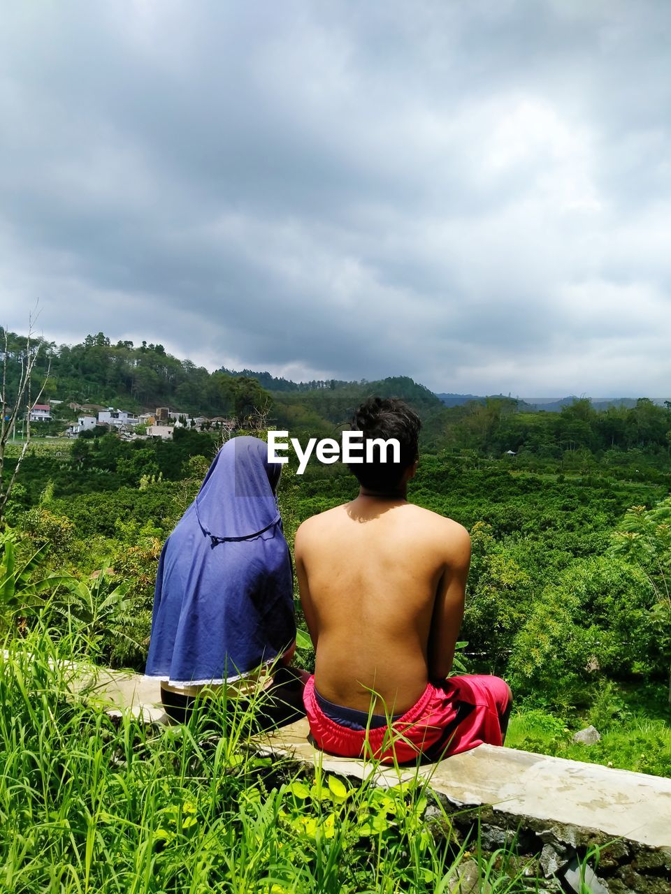 Rear view of shirtless man sitting on field