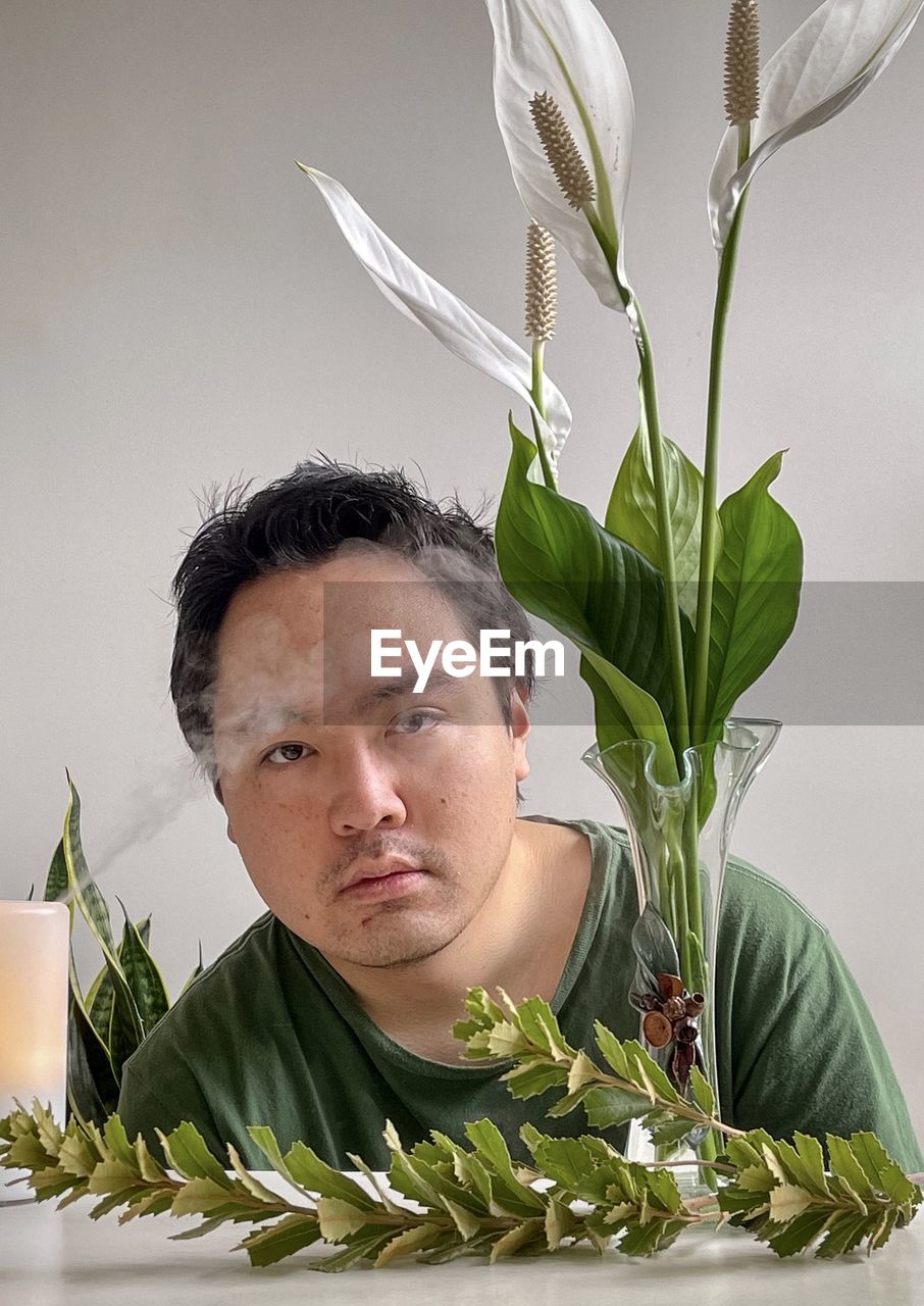 Portrait of young asian man with aromatherapy diffuser, peace lilies in vase and branches.