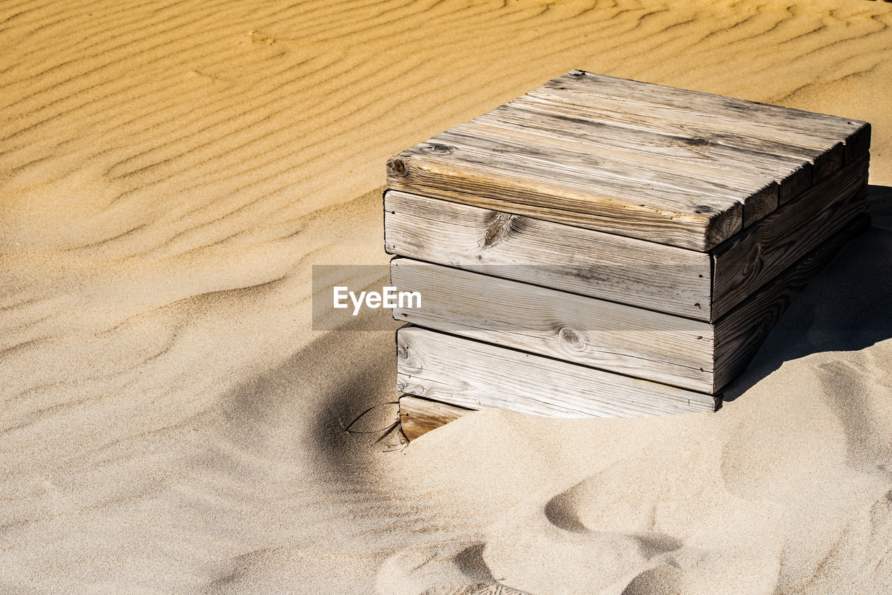 A close up shot of a single wooden box being consumed slowly by the sand in bolonia, spain