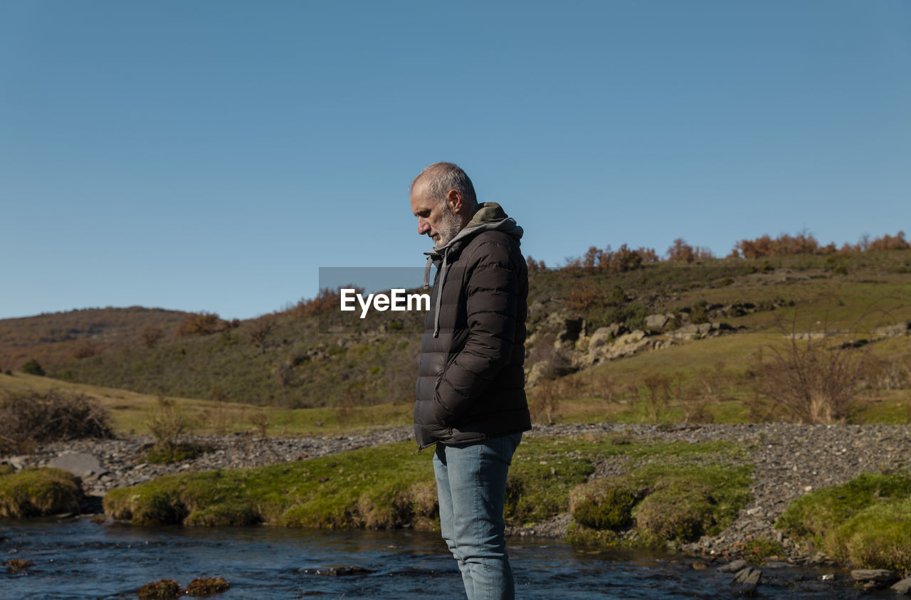 Portrait of adult man in countryside with river against blue sky, in guadalajara, spain